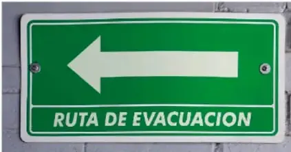Fotografía de una señal verde de seguridad con flecha blanca y el texto «RUTA DE EVACUACIÓN».