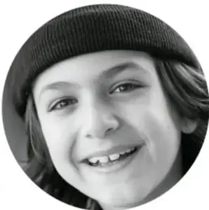 Fotografía circular en blanco y negro de un niño sonriente con gorro (gorro tejido) mirando a la cámara.
