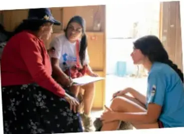 Fotografía de tres personas conversando en un entorno comunitario, una de ellas con una tabla de apuntes.