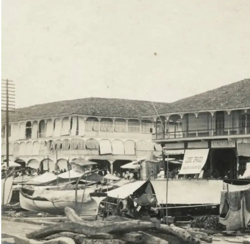 Fotografía histórica del puerto de Guayaquil a finales del siglo XIX. Se observan embarcaciones, puestos comerciales y edificios alrededor del puerto.