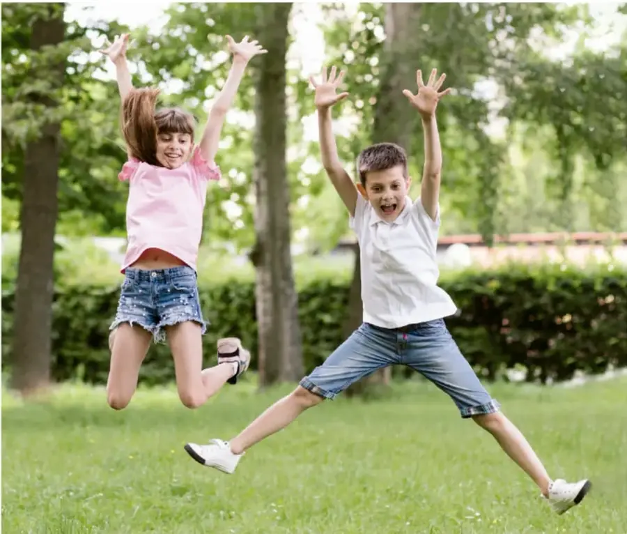Fotografía de dos niños saltando con los brazos en alto en un parque, expresando alegría.
