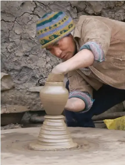 Artesano alfarero moldeando una vasija de barro en un torno primitivo, representando la artesanía y la tecnología antigua.