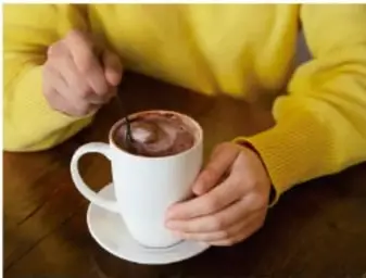 Persona con suéter amarillo tomando una bebida caliente en taza blanca, ilustrando la conducción.