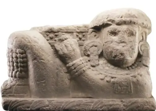 Escultura de piedra de un hombre recostado con brazos cruzados y cabeza girada hacia el frente.