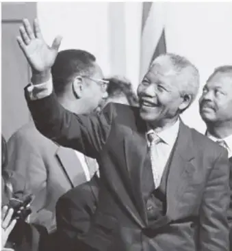 Nelson Mandela saludando con la mano, acompañado de otras personas, en un acto público.