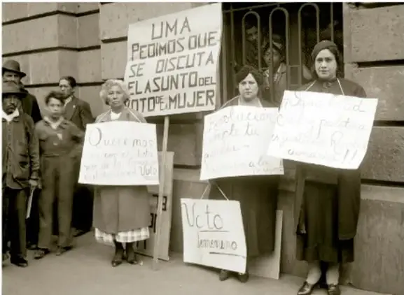 Fotografía en blanco y negro de un grupo de mujeres sosteniendo carteles que dicen 'LIMA PEDIMOS QUE SE DISCUTA EL ASUNTO DE LA MUJER' y 'VOTO FEMENINO', en una protesta por el sufragio femenino.