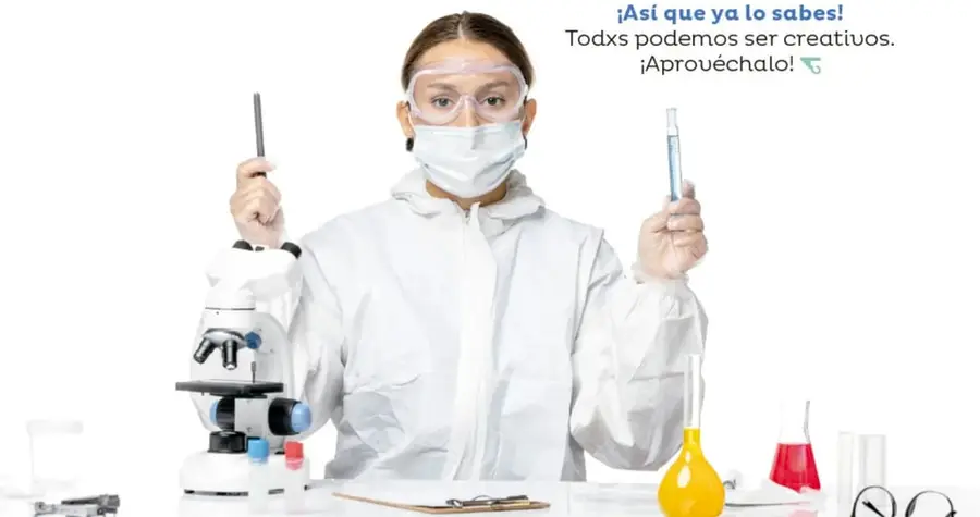 Fotografía de una científica con bata blanca, careta y goggles de laboratorio, sosteniendo un tubo de ensayo, con microscopio y matraces de colores sobre la mesa.