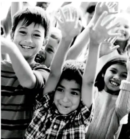 Fotografía en blanco y negro de un grupo de niños y niñas sonrientes que levantan las manos, representando la participación y el entusiasmo de organizarse en comunidad.