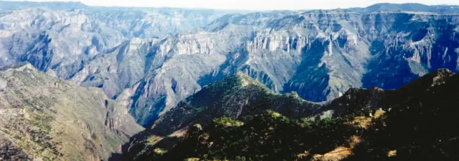 Panorámica de las Barrancas del Cobre: montañas escarpadas, profundas cañadas, paredes rocosas y laderas cubiertas de vegetación.