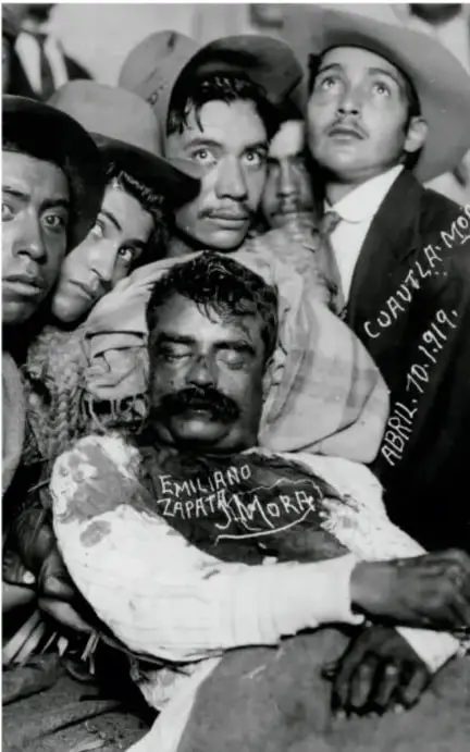 Fotografía en blanco y negro del cadáver de Emiliano Zapata, rodeado de varias personas. Sobre la imagen se lee 'EMILIANO ZAPATA MOR.' y 'ABRIL 10 1919'.