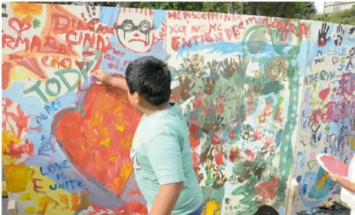 Niño de camiseta verde pintando con la mano un mural colorido con un corazón y leyendas como 'Diversidad', 'Cariño' y 'Todos'.