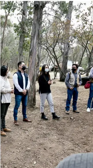 Fotografía de un grupo de jóvenes estudiantes con mascarillas, de pie en un área boscosa, aparentemente en actividad al aire libre o de campo.