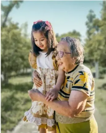Foto de una abuela mayor abrazando a una niña pequeña al aire libre, entre árboles, posiblemente Pachita y su nieta.