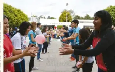 Fotografía de estudiantes y docente en patio escolar durante actividad grupal; una estudiante sostiene un globo rosa.