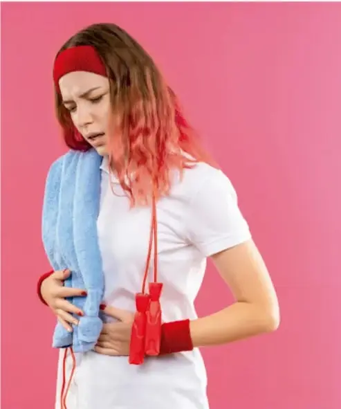 Fotografía de una joven deportista con gorro y toalla, con expresión de dolor y la mano en el abdomen, ilustrando el malestar menstrual durante la actividad física.