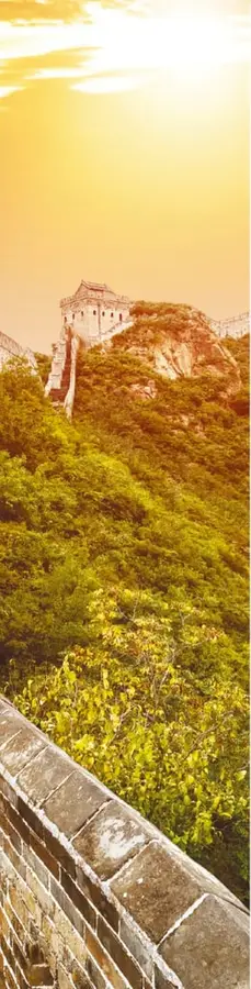 Fotografía vertical de la Gran Muralla serpenteando por una montaña con vegetación otoñal amarilla, al atardecer.