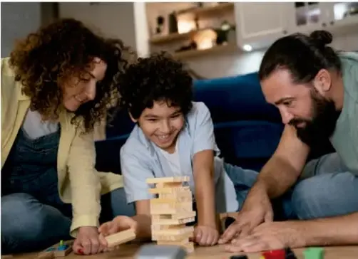 Fotografía de una familia (madre, hijo e hijo) jugando en equipo con bloques de madera en el suelo.