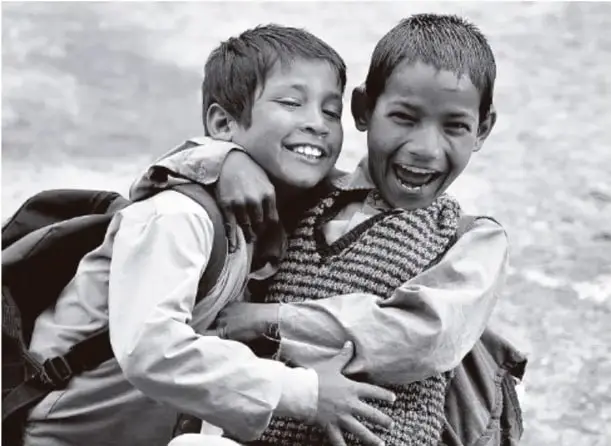Fotografía en blanco y negro de dos niños que se abrazan riendo, uno con mochila, transmitiendo alegría y amistad.