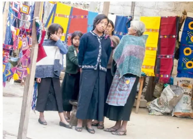 Fotografía de mujeres indígenas junto a telas y artesanías de colores en un espacio de venta, con crédito: FAO, corte de EE COI.