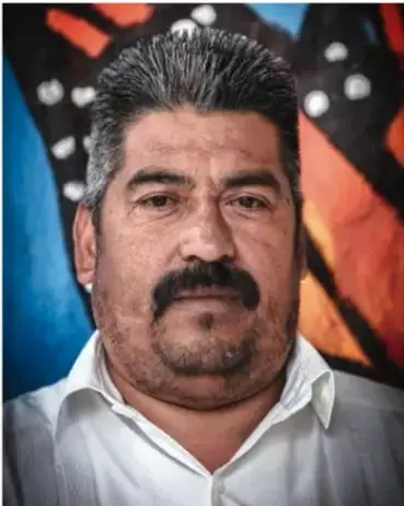 Fotografía de Homero Gómez González, hombre con bigote y camisa blanca, frente a un fondo colorido.