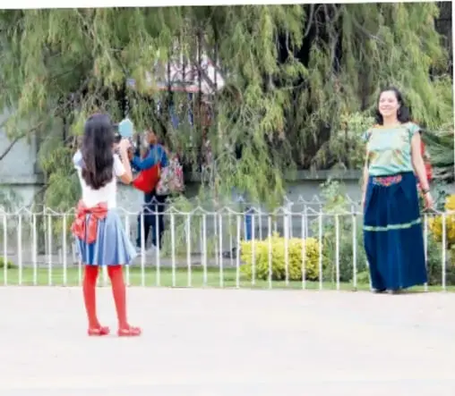Estudiantes tomando fotografías durante una actividad al aire libre en la escuela, con una persona con vestimenta tradicional al fondo.