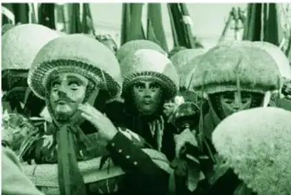 Fotografía a color de danzantes Parachicos: máscaras de madera tallada que simulan rostros humanos, monteras altas de fibra natural, sarapes con chalinas bordadas y sonajas de hojalata; al fondo más cabezas con monteras.