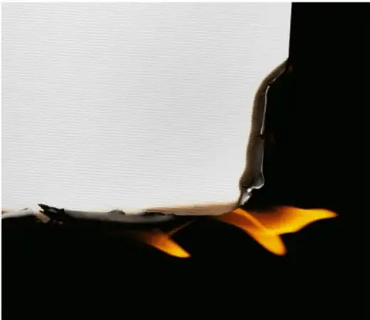 Fotografía de una hoja de papel ardiendo sobre un fondo oscuro; la llama naranja avanza por el borde y deja cenizas negras.
