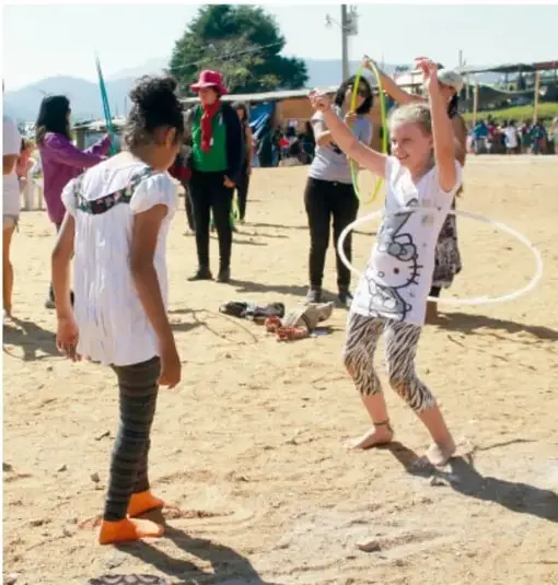 Fotografía de niños y adultos en un espacio al aire libre (arena) realizando actividad física con aros y moviéndose, en contraste con la conducta sedentaria.
