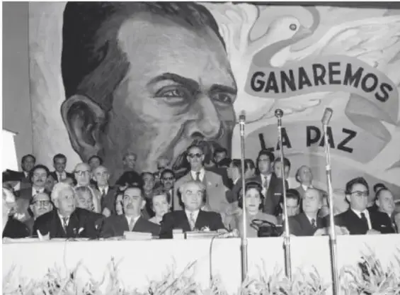 Fotografía histórica en blanco y negro de una asamblea con un mural que muestra el rostro de un líder y el texto «GANAREMOS LA PAZ», evocando la lucha por la paz en México