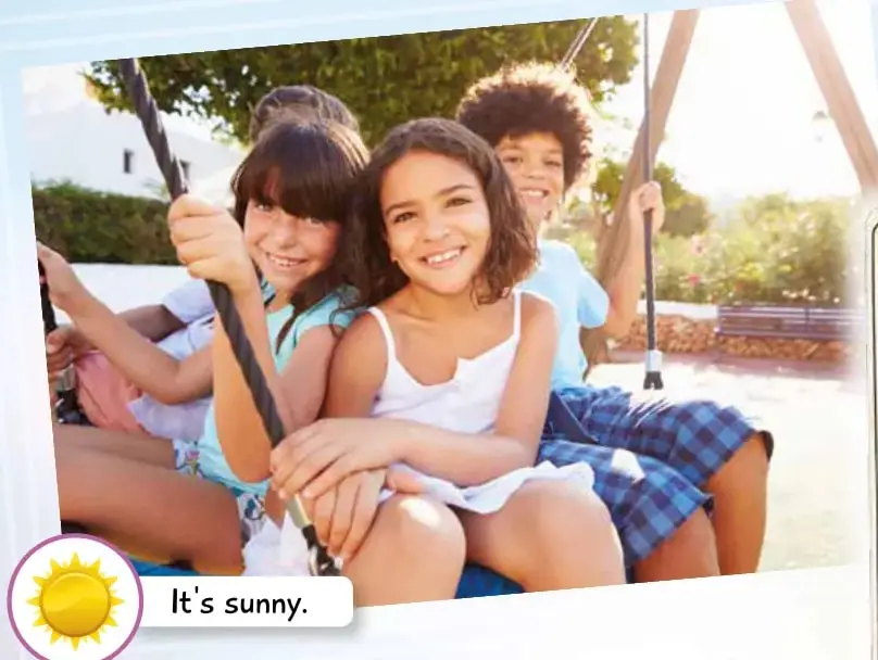 Tres niños sonrientes sentados en un columpio en un día soleado. Ícono de sol y texto 'It's sunny.'