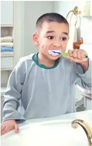 Fotografía de un niño cepillándose los dientes frente al espejo del baño, con la llave del lavamanos cerrada.