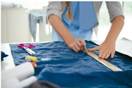 Persona midiendo una tela azul con una regla sobre una mesa de trabajo.