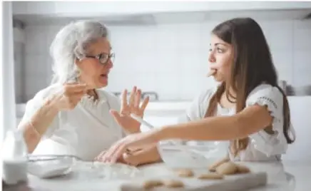 Fotografía de una abuela y su nieta conversando en una cocina mientras preparan galletas.