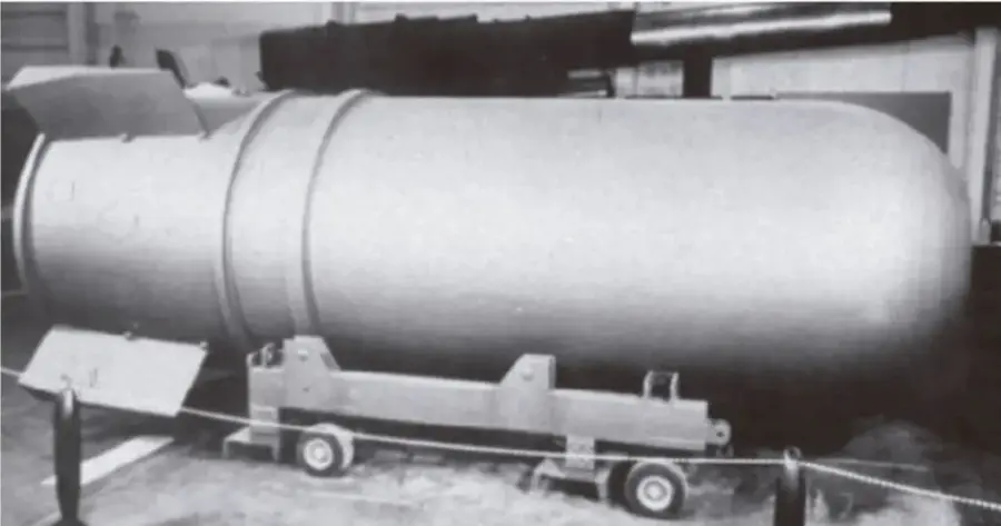 Fotografía en blanco y negro de un misil o bomba de gran tamaño montado sobre un carro de transporte con ruedas, exhibido en un museo o instalación militar.