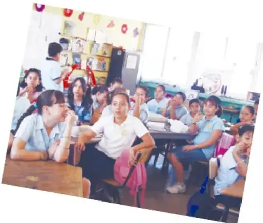 Grupo de estudiantes de primaria sentados en el aula, algunos levantan la mano.