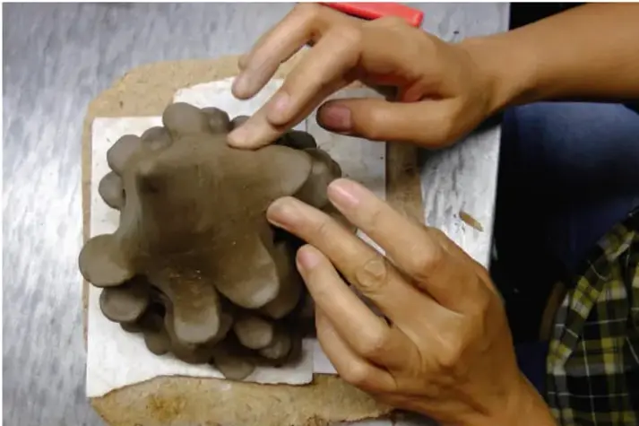 Fotografía de las manos de un estudiante moldeando una figura de barro o plastilina sobre una base de madera, como ejemplo de trabajo manual dentro de un proyecto de aula.