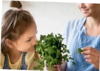 Fotografía de una niña y una mujer adulta manipulando plantas medicinales verdes, en un contexto de aprendizaje familiar.