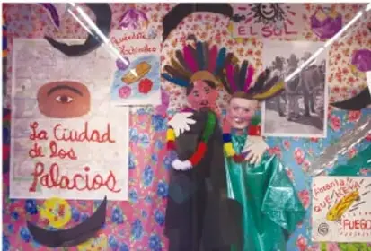 Fotografía de estudiantes disfrazados junto a un mural o póster titulado 'La Ciudad de los Palacios', con adornos de papel picado y elementos culturales, que ilustra un proyecto escolar terminado.