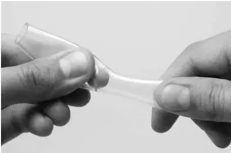 Fotografía en blanco y negro de dos manos sosteniendo y apretando una manguera transparente flexible, con una bolita en su interior, modelando el movimiento peristáltico del tubo digestivo.