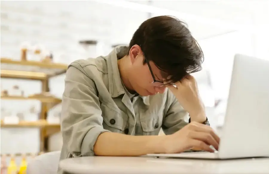 Fotografía de un adolescente sentado frente a una computadora portátil, con la cabeza apoyada en la mano y expresión de cansancio o preocupación, ilustrando el estrés o malestar propio de esta etapa.