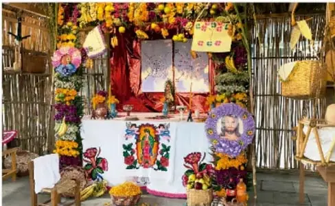 Fotografía de una ofrenda o altar de Día de Muertos adornada con cempasúchil, papel picado, comidas y fotografías.