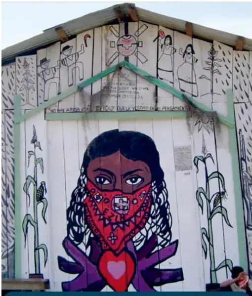 Mural en una pared de madera con una mujer indígena con pasamontañas y corazón, acompañado de la frase 'No hay arma más eficaz que la verdad en el pensamiento, Caracol Oventic, Chiapas, 2007'.