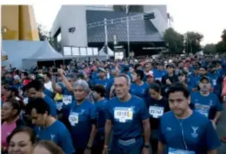 Grupo grande de personas con camisetas azules participando en una actividad deportiva comunitaria al aire libre.
