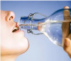 Fotografía de una persona bebiendo agua directamente de una botella de vidrio, como ejemplo de hidratación saludable.