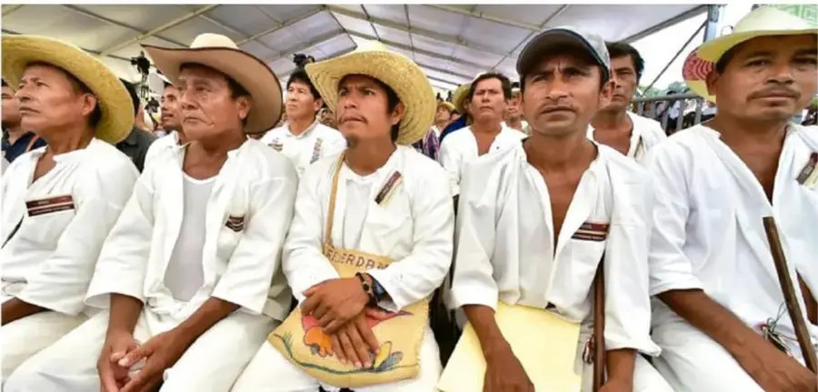 Fotografía de un grupo de hombres indígenas con sombreros de paja o escopetas, sentados en un espacio comunitario, posiblemente durante una asamblea o ceremonia.