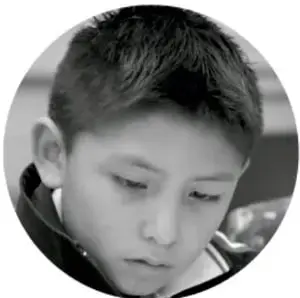 Fotografía circular en blanco y negro de un niño de primaria con la mirada baja, pensativo.