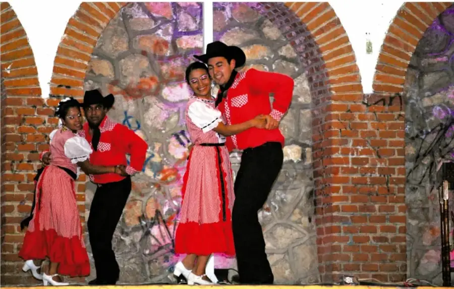 Parejas bailando danza tradicional frente a muros de ladrillo.
