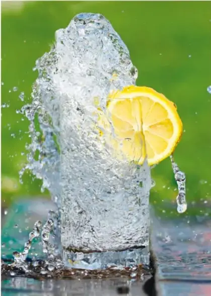 Fotografía de un vaso de agua con hielo y una rodaja de limón, con salpicaduras de agua.