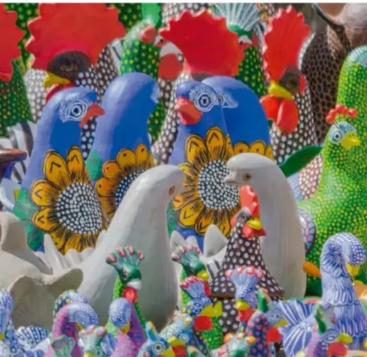 Fotografía de figuras de cerámica y talla popular mexicana pintadas de colores vivos (aves, gallos, girasoles), que ilustran las manifestaciones artísticas artesanales del país.