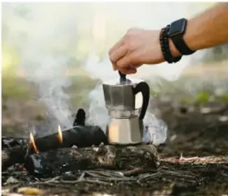 Fotografía de una persona calentando una cafetera sobre una fogata.